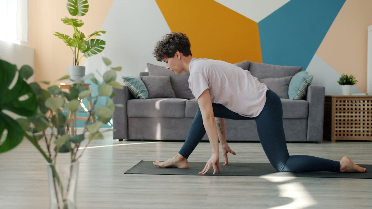 Woman doing yoga on a mat in a living room.